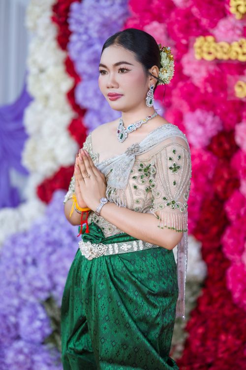 Free A woman in traditional Khmer dress stands amidst vibrant flowers in a Cambodian celebration. Stock Photo