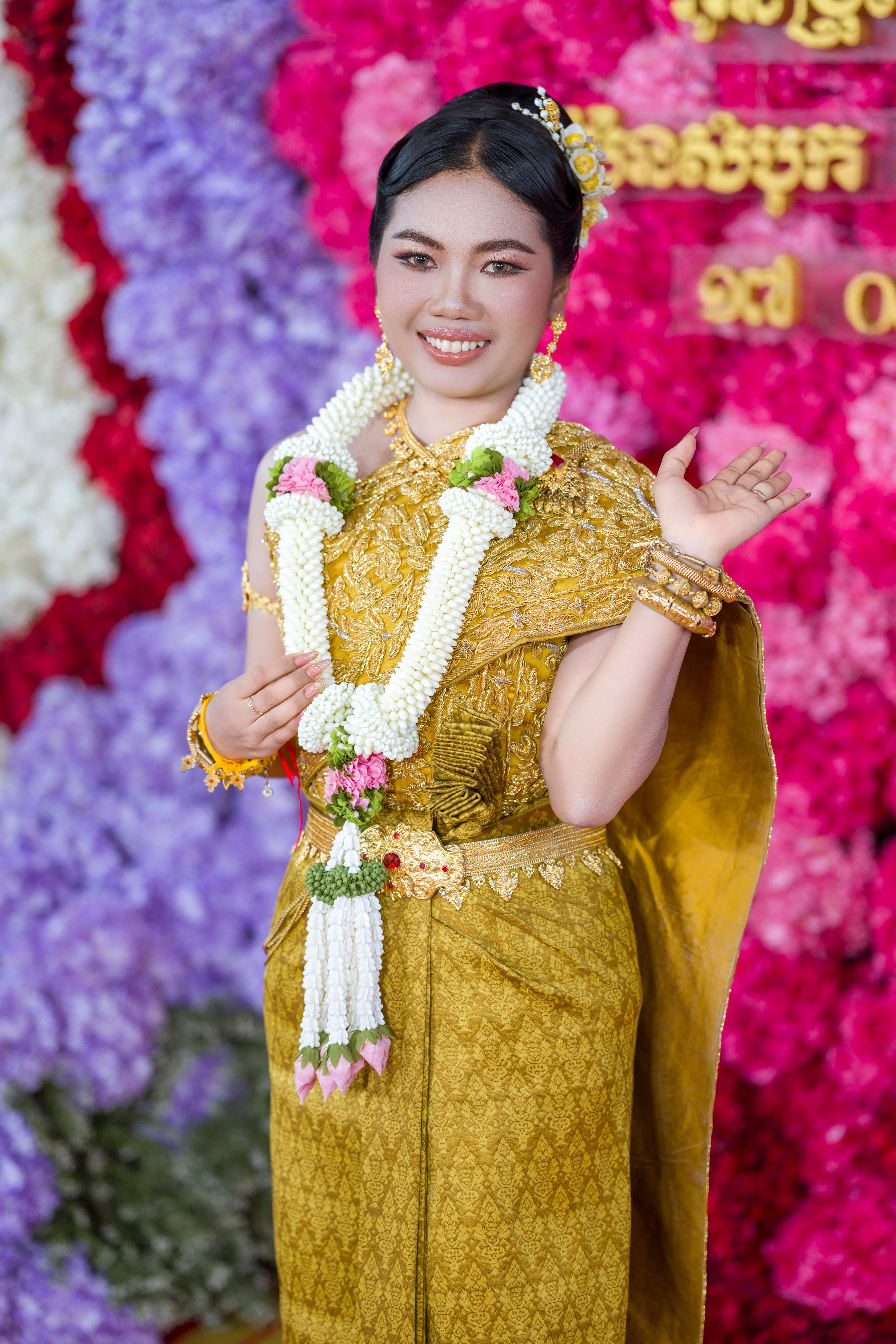 A woman in traditional Cambodian attire at a wedding ceremony with floral backdrop.