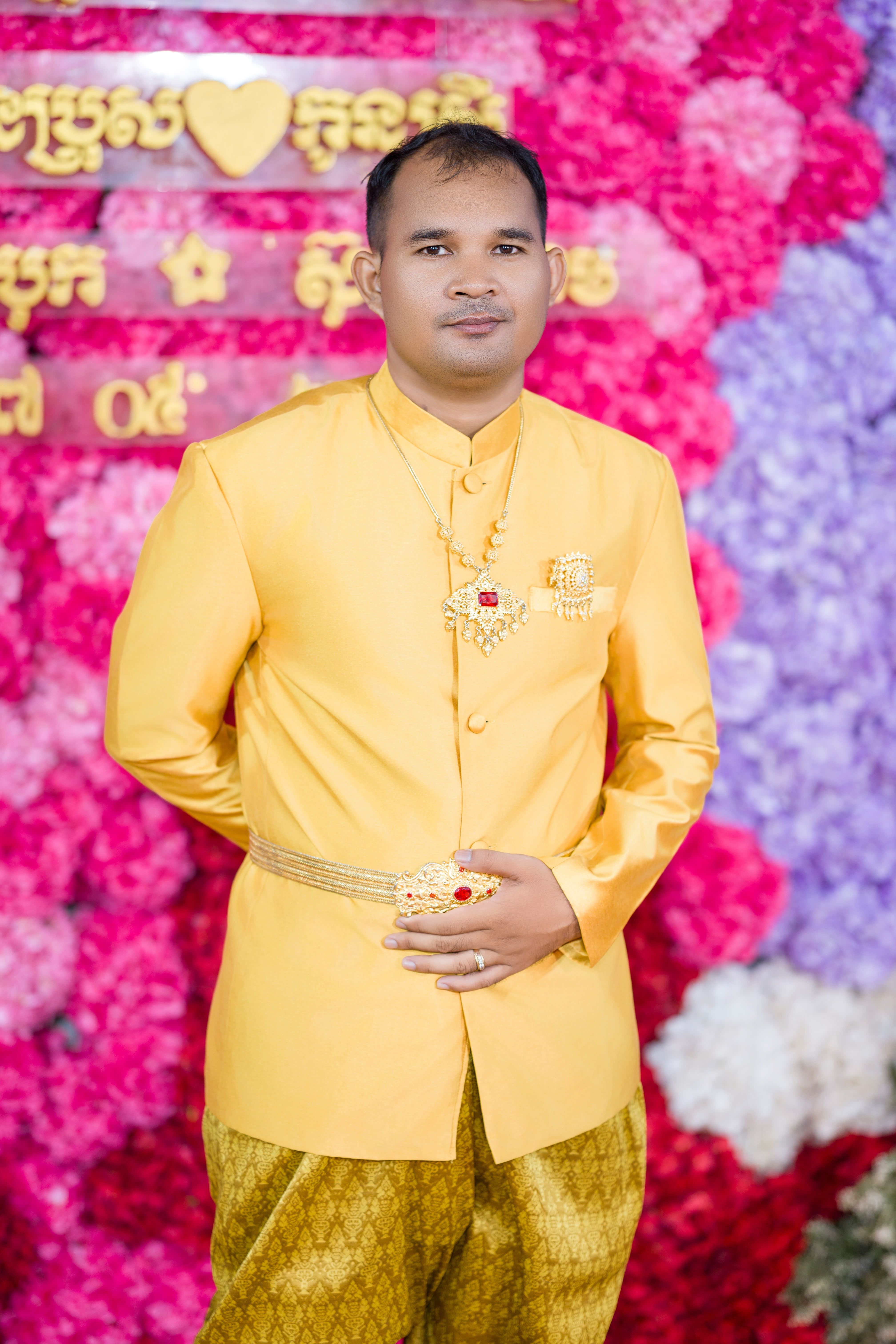 Elegant Cambodian groom in traditional attire at a vibrant floral wedding ceremony.