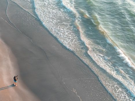 Aerial view of a solitary figure walking on the shoreline in Corpus Christi, Texas with gentle waves along the beach.