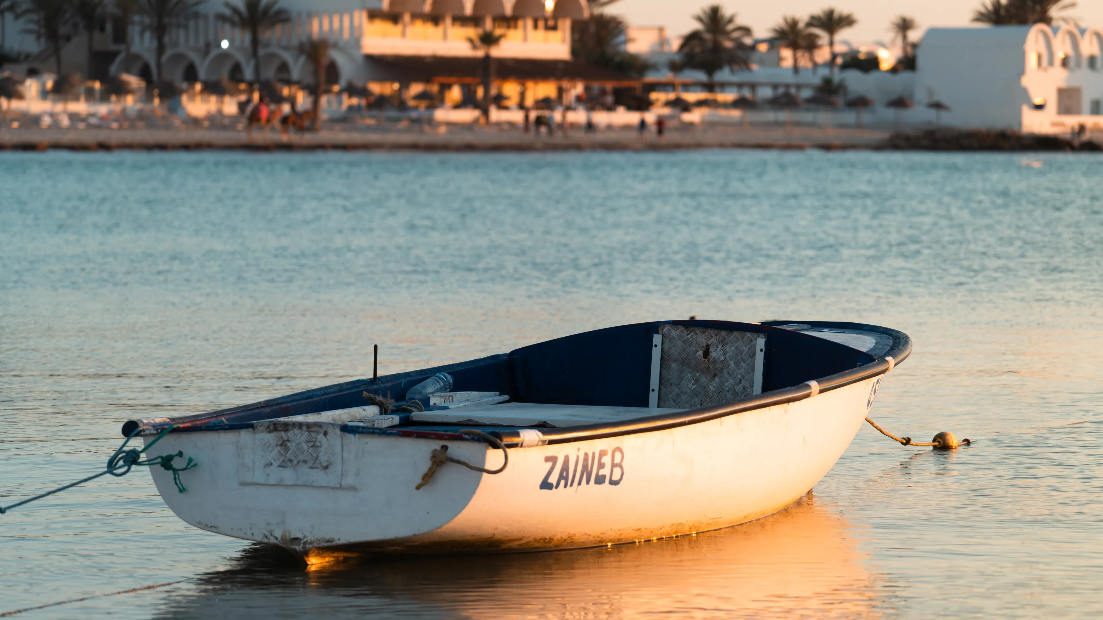 A serene fishing boat floats on calm waters at sunset in Médenine, Tunisia, reflecting warm golden hues.