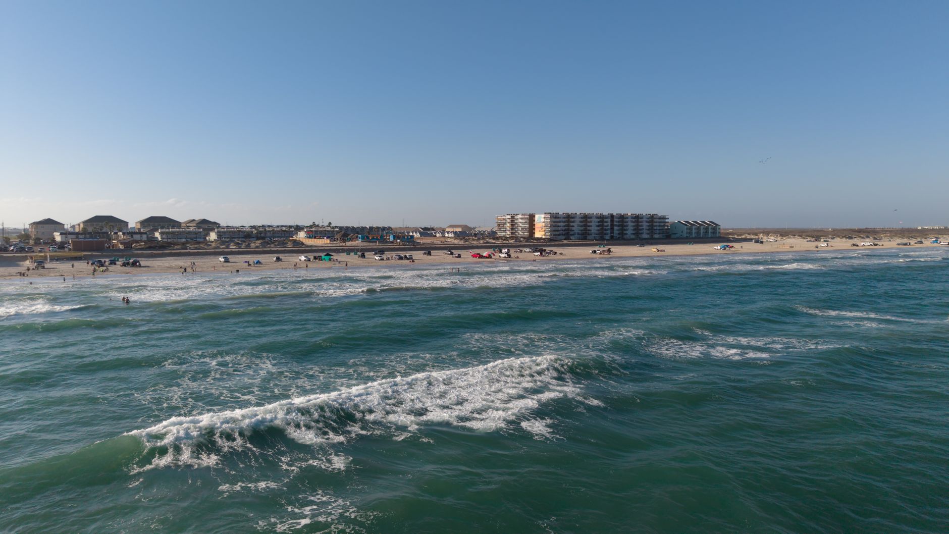 north coast beach event organizer — Aerial view of a sunny beach in Corpus Christi with waves and coastal buildings.