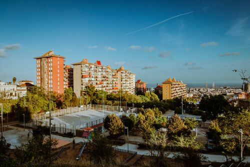Free A scenic urban view of Barcelona featuring residential buildings, trees, and a sports court under a clear blue sky. Stock Photo