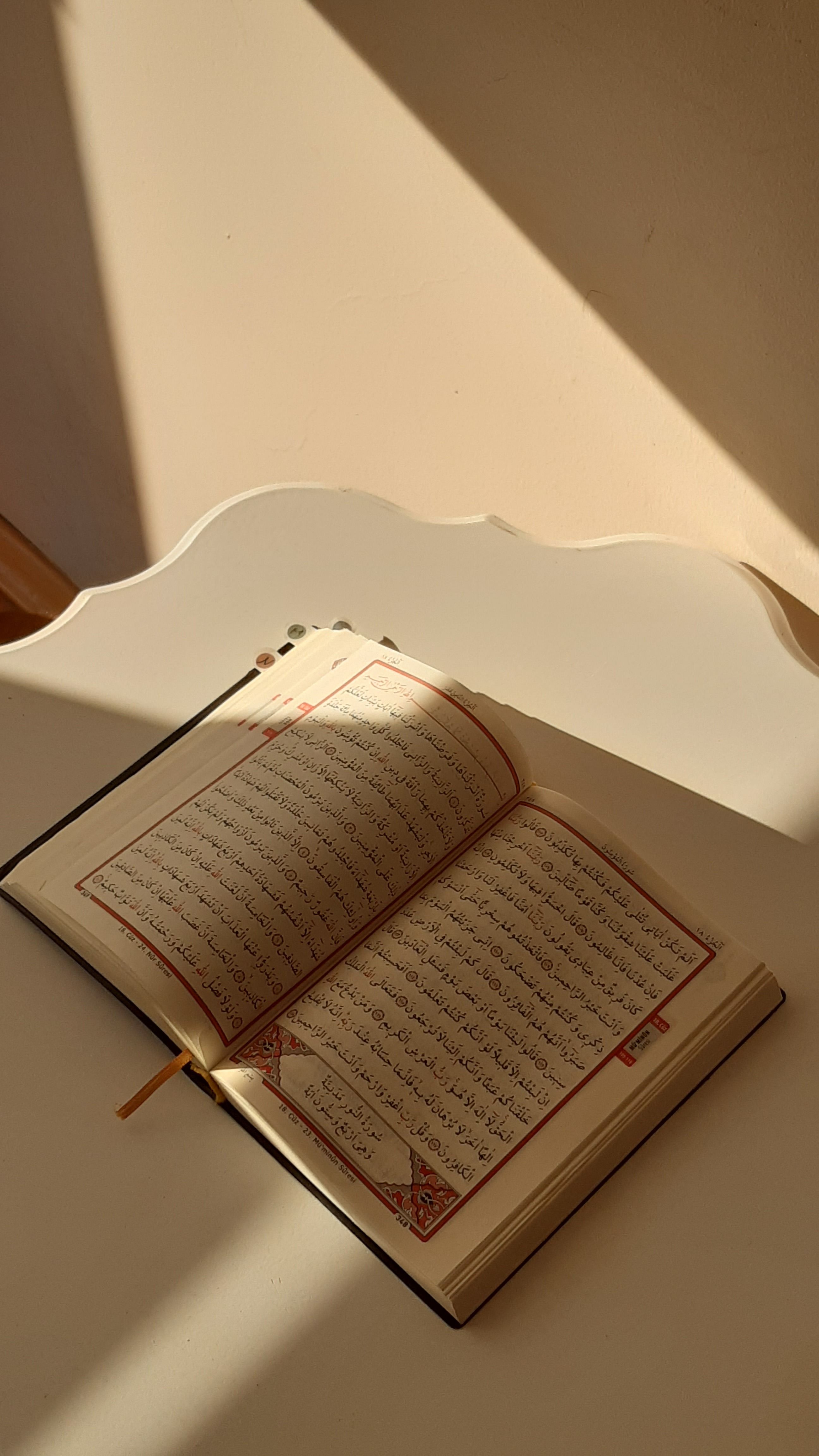 An open Quran receives warm sunlight on a clean, white desk, creating a serene atmosphere.