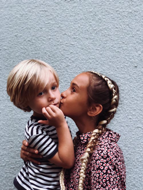 A Girl Kissing a Young Boy in the Cheeks