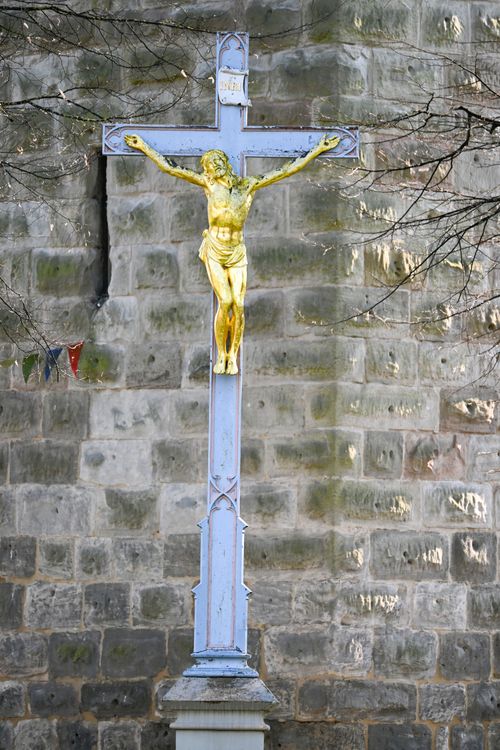 Free A gold crucifix stands prominently against a textured stone wall in Baden-Württemberg, Germany. Stock Photo