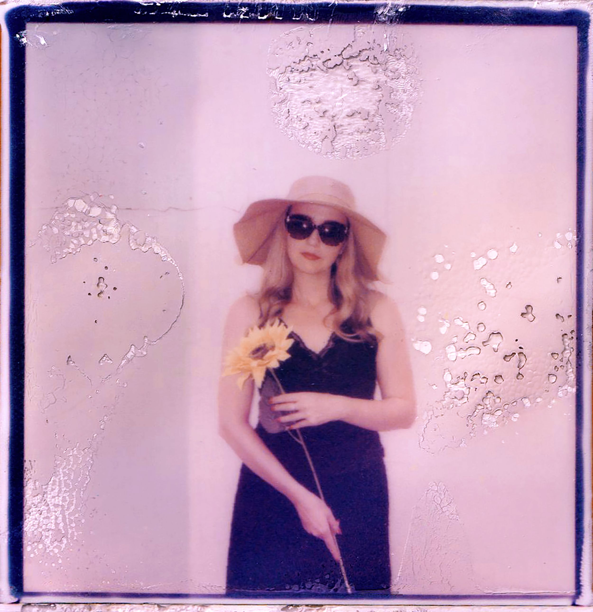 Artistic polaroid of woman in sunglasses holding sunflower, vintage style.