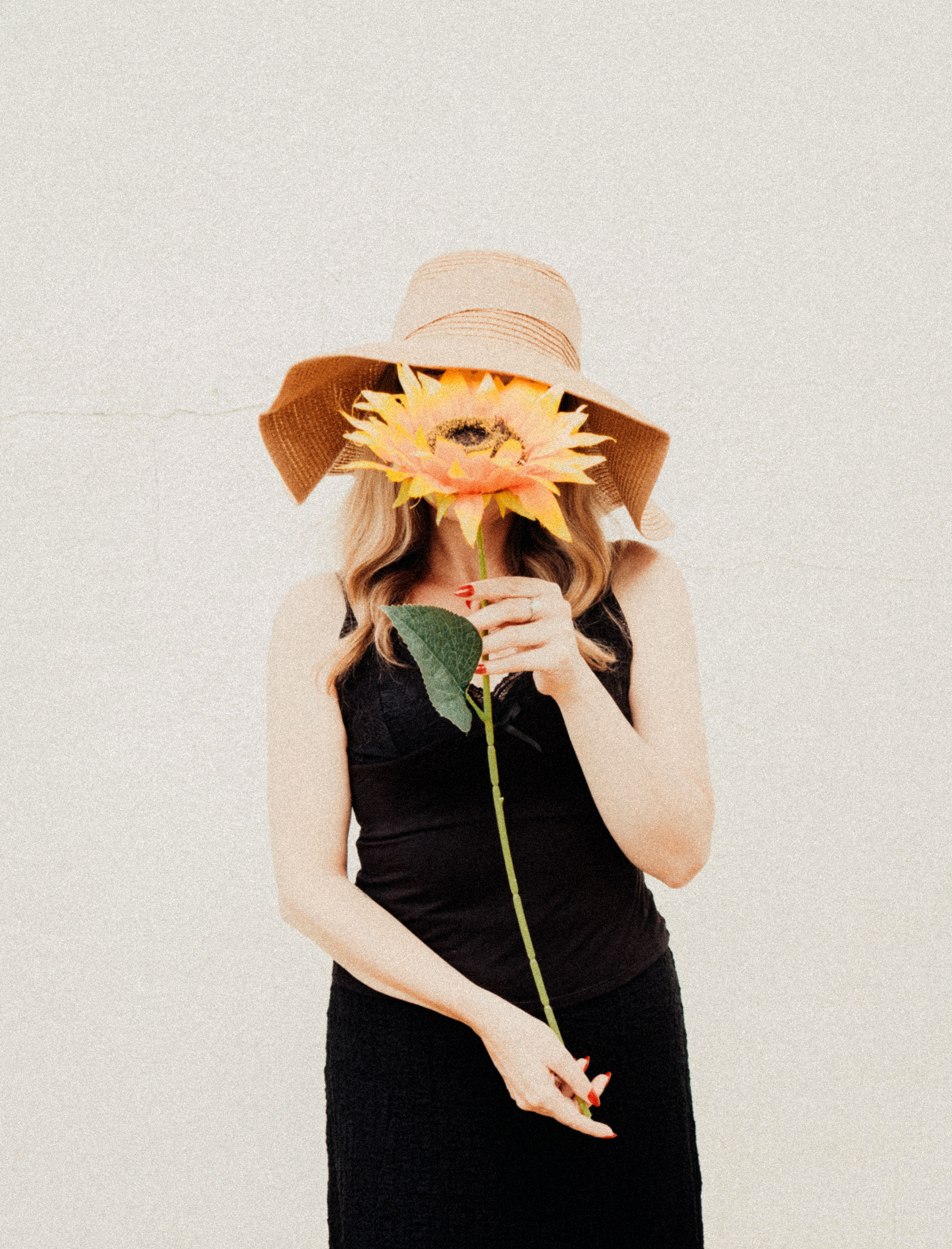Stylish woman in hat holding sunflower against a plain background. Artistic and summery vibe.