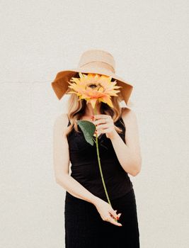 Stylish woman in hat holding sunflower against a plain background. Artistic and summery vibe.