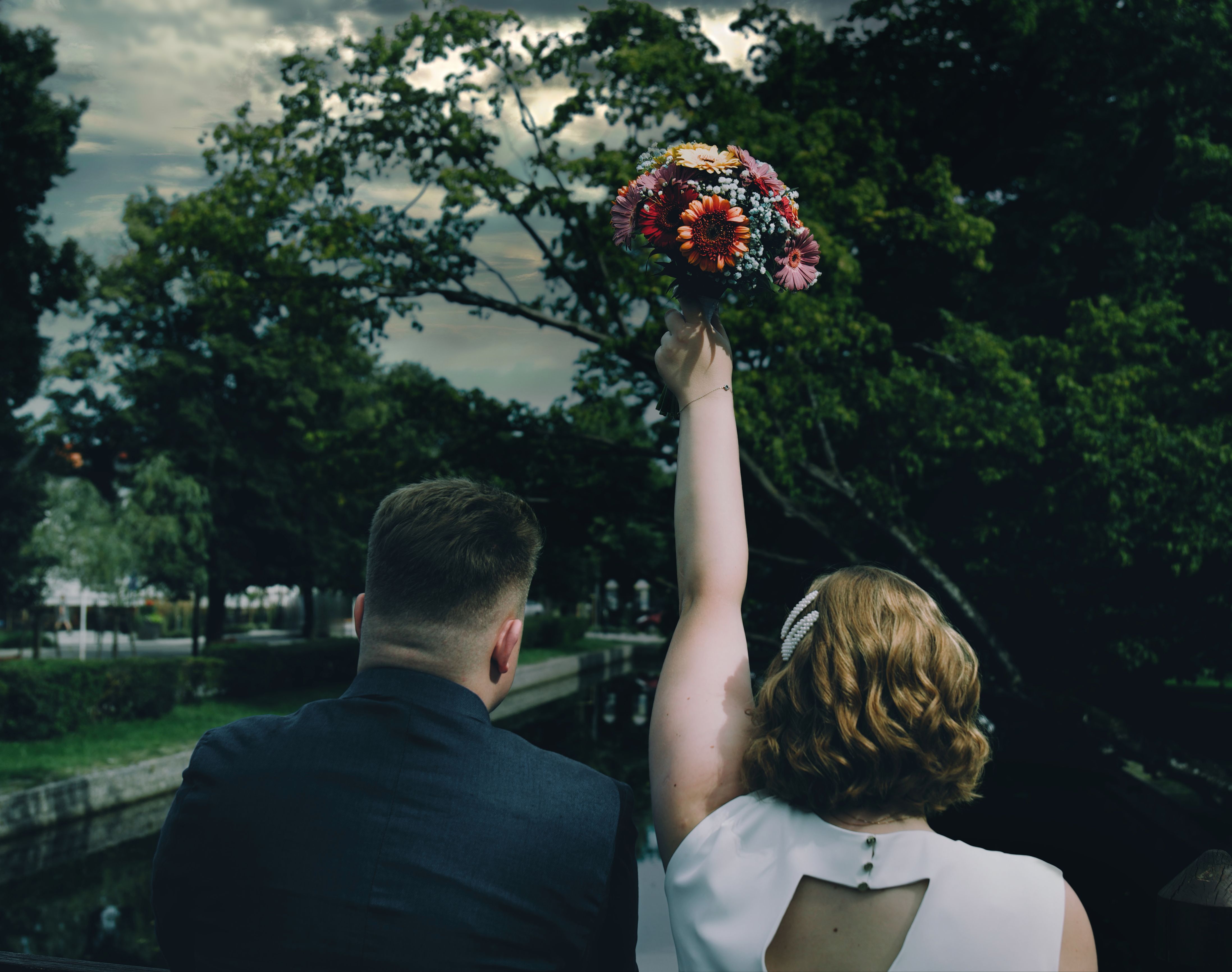 A bride joyfully raises her bouquet outdoors, capturing a romantic wedding moment.