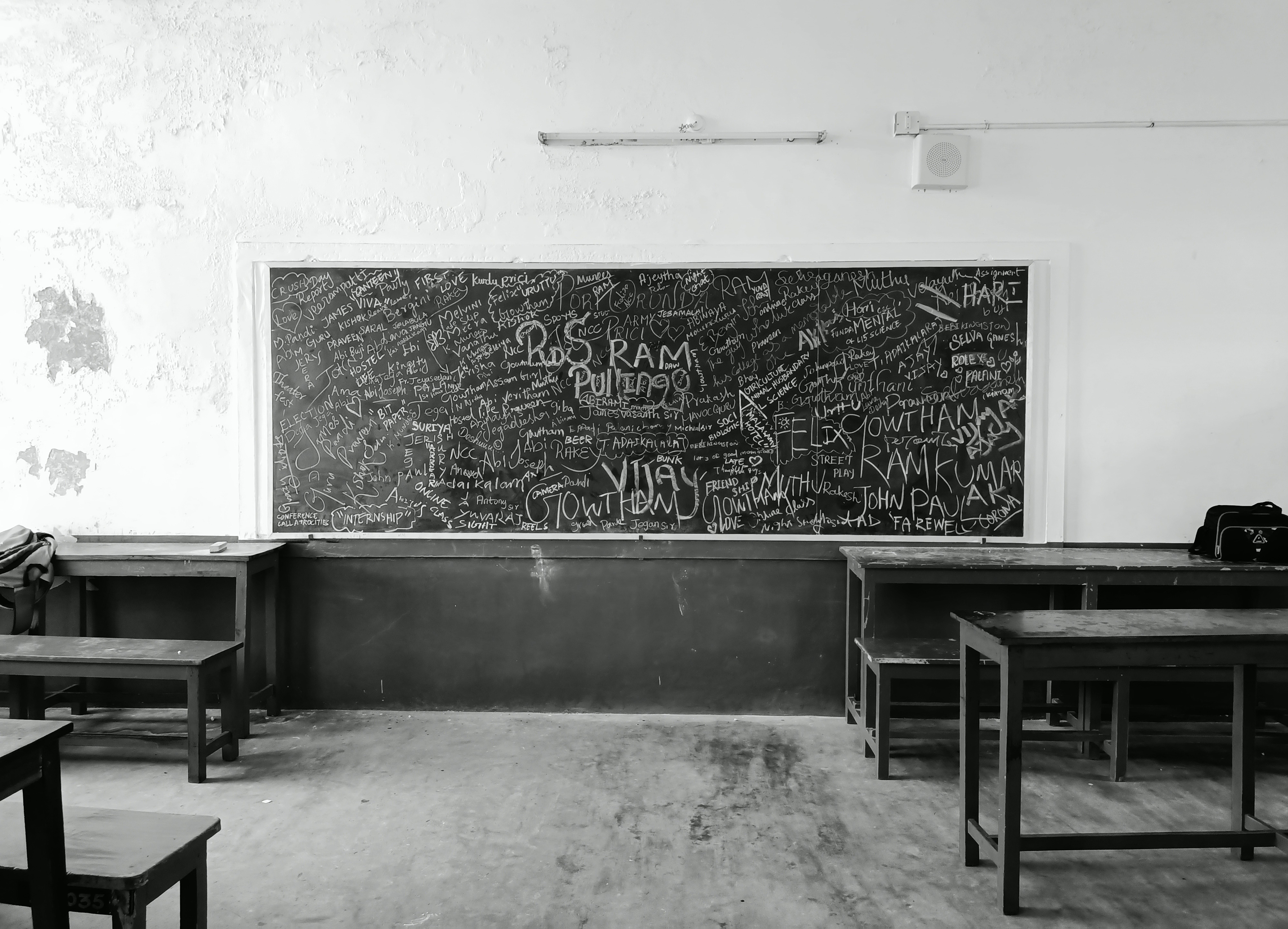 A nostalgic black and white photo of an empty classroom in Madurai, India, featuring a graffiti-covered chalkboard.