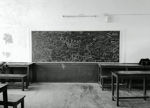 Free A nostalgic black and white photo of an empty classroom in Madurai, India, featuring a graffiti-covered chalkboard. Stock Photo