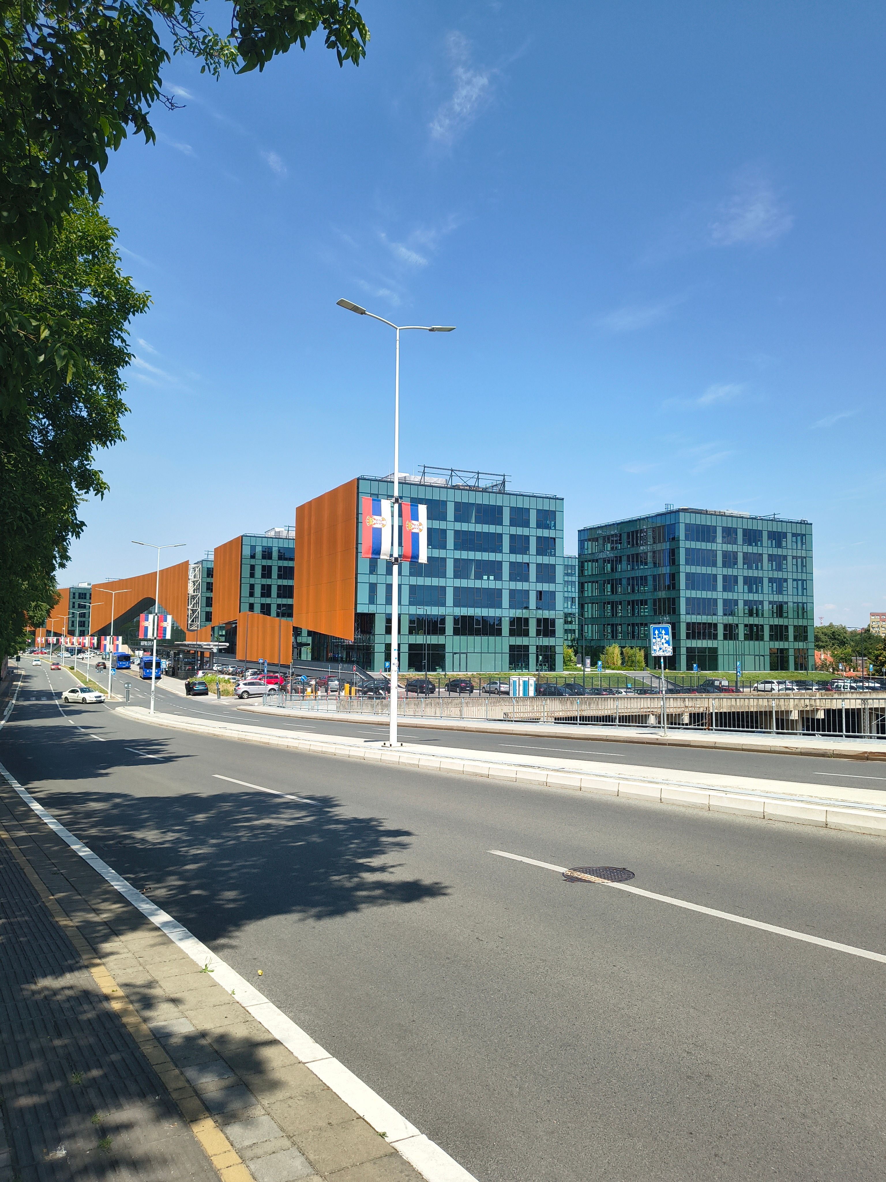Contemporary office buildings with glass facades line a quiet urban street under a clear blue sky.
