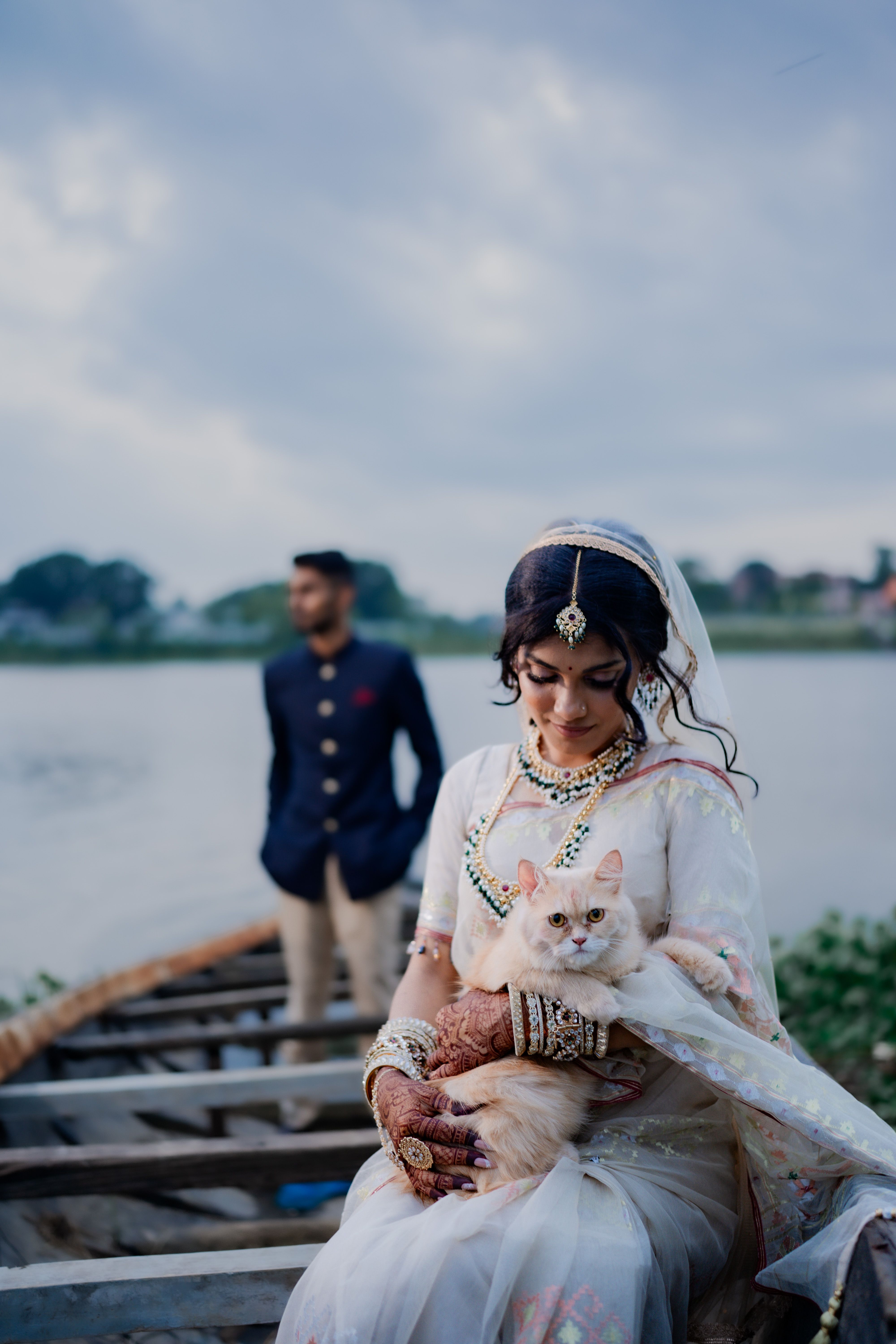 A traditional Bangladeshi wedding scene with a bride holding a cat on a boat near a river.