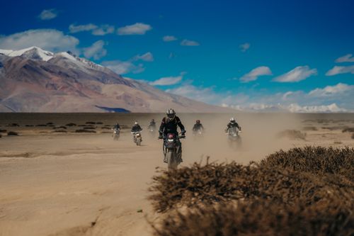 Free Group of motorcyclists riding through a dusty desert landscape under a clear blue sky. Stock Photo