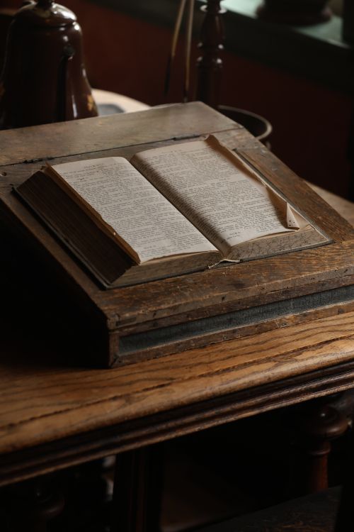 Free An open antique book displayed on a rustic wooden stand, evoking a vintage library atmosphere. Stock Photo