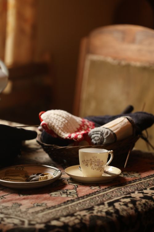 Free Warm and inviting indoor setting featuring a tea cup and knitted items on a patterned tablecloth. Stock Photo