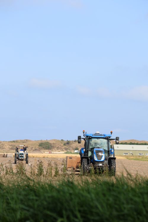 Free Two tractors working on a field under a clear blue sky, capturing rural agriculture. Stock Photo
