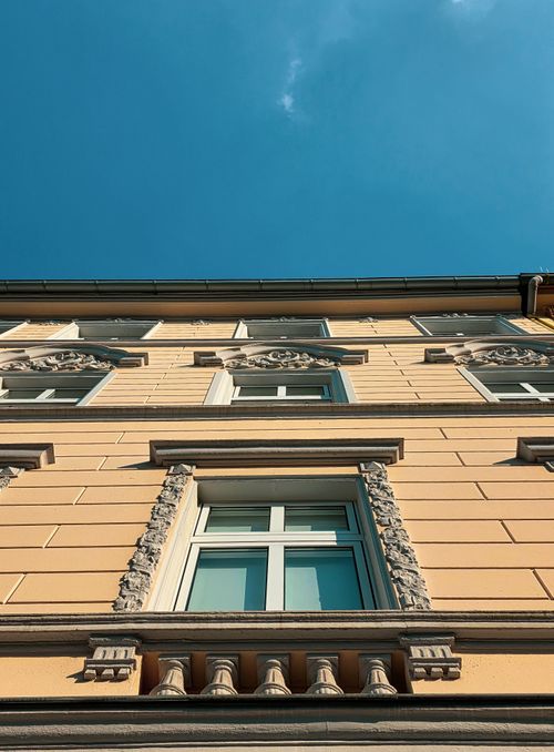 Free Upward view of a classic European building facade against a clear blue sky, showcasing architectural details. Stock Photo