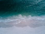 这张航拍照片令人惊叹，碧绿色的海浪冲刷着原始沙滩，非常适合用作背景