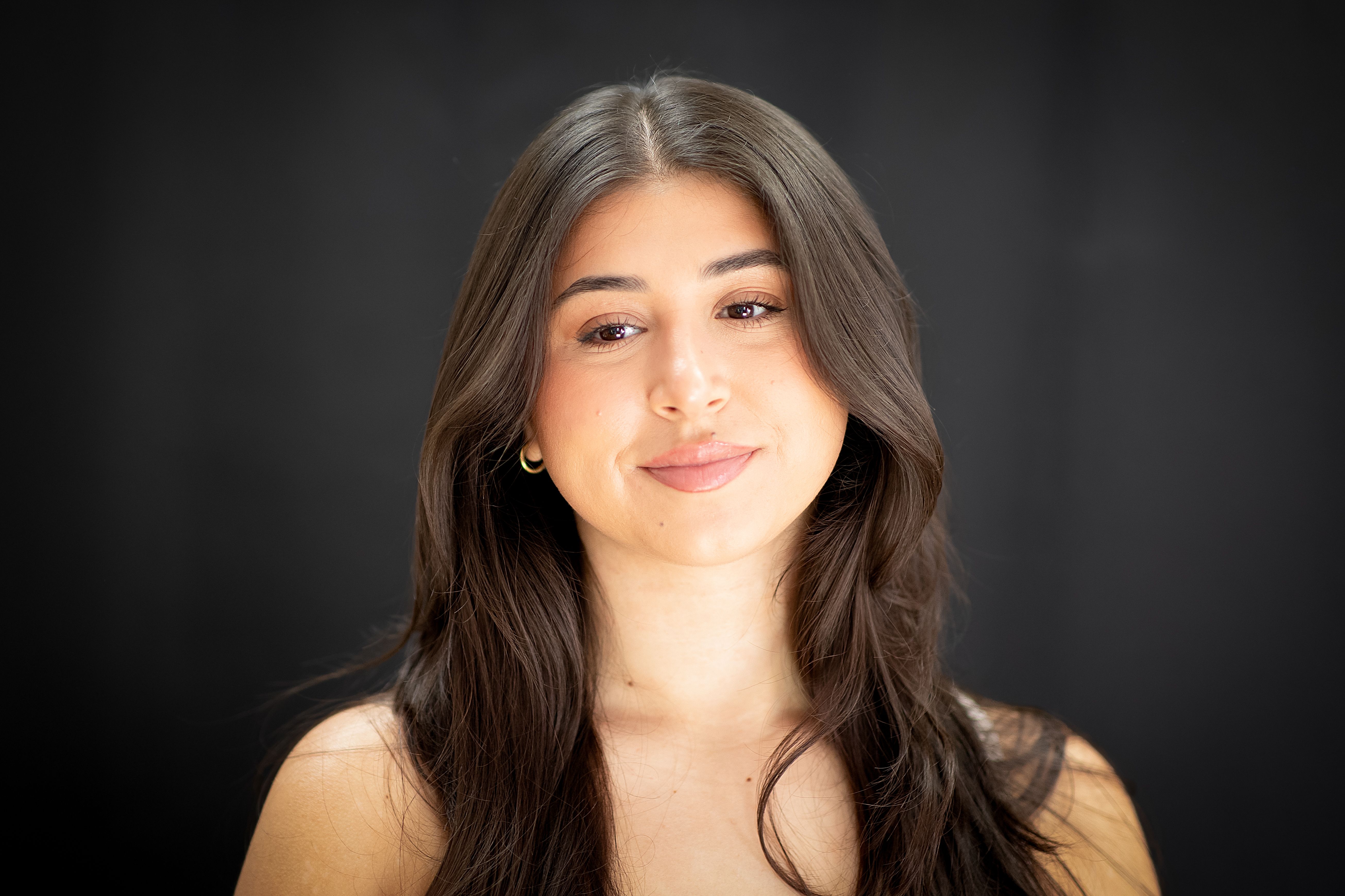 Close-up portrait of a young woman with long dark hair and a gentle expression against a black background.