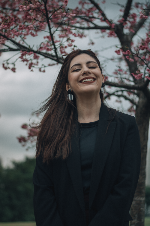 Free A woman smiling under cherry blossom trees in a relaxed outdoor scene. Stock Photo