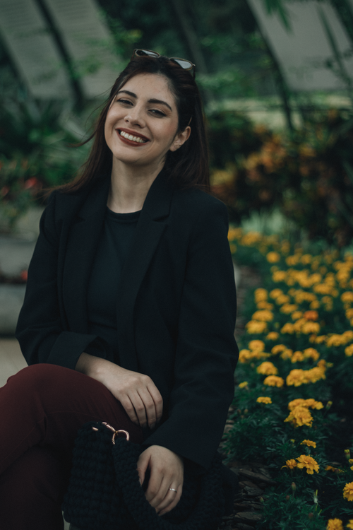 Free Portrait of a smiling woman sitting in a garden with vibrant yellow flowers. Stock Photo