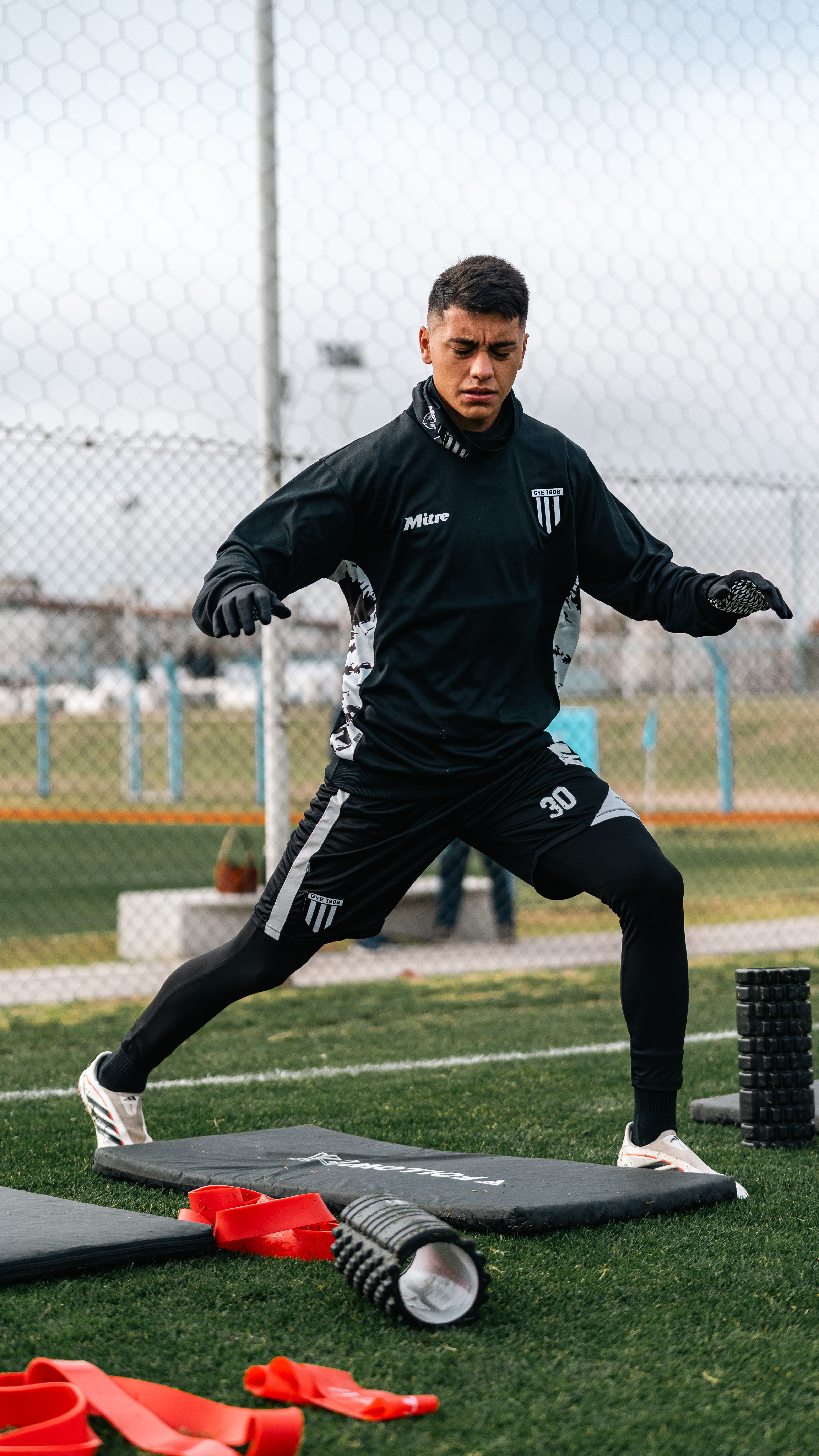 Dynamic portrait of a young male athlete warming up outdoors with resistance bands and foam rollers.