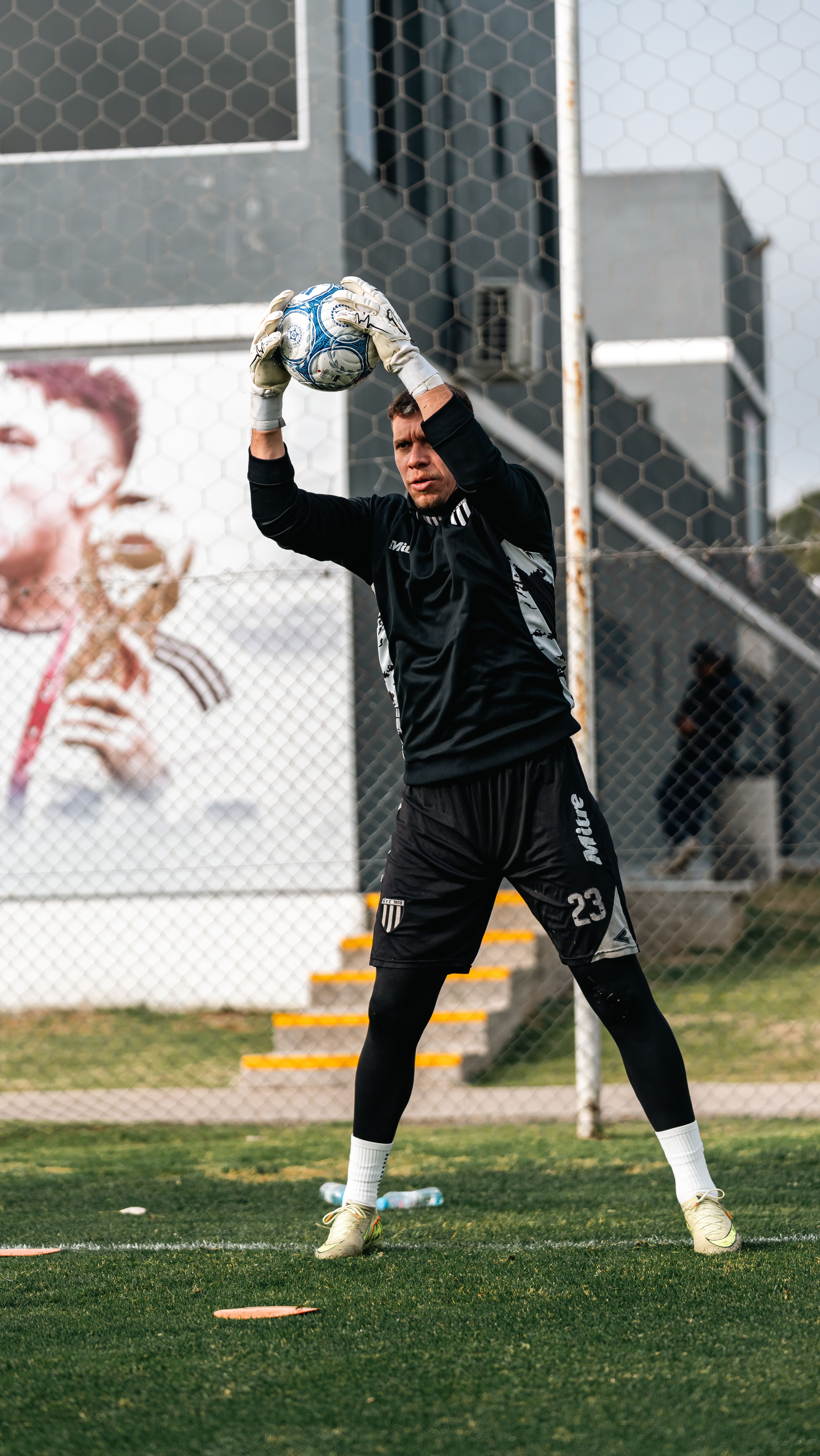 Soccer goalkeeper practicing catching drills on urban sports ground.