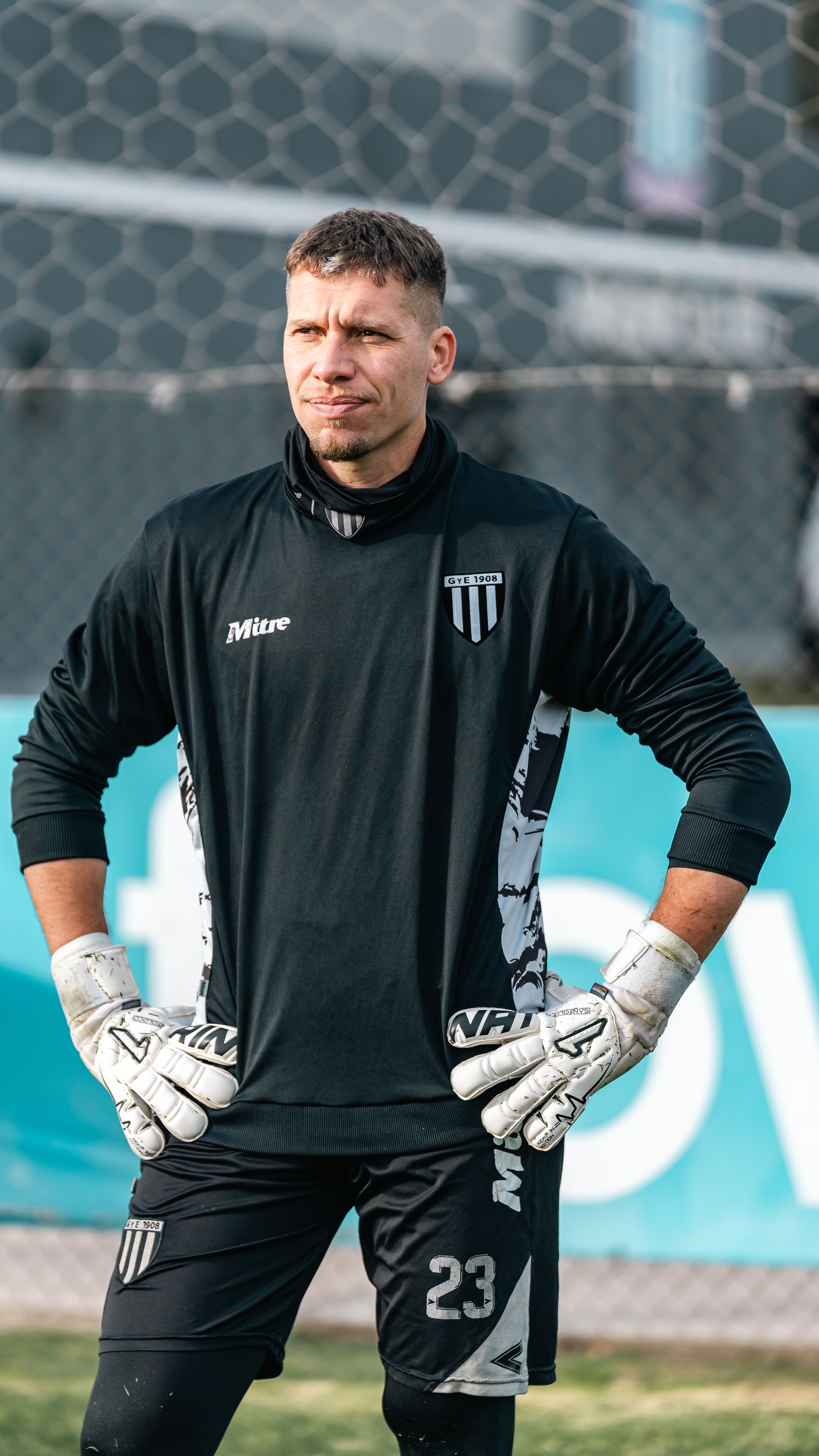 Focused soccer goalkeeper wearing black training uniform and gloves outdoors.