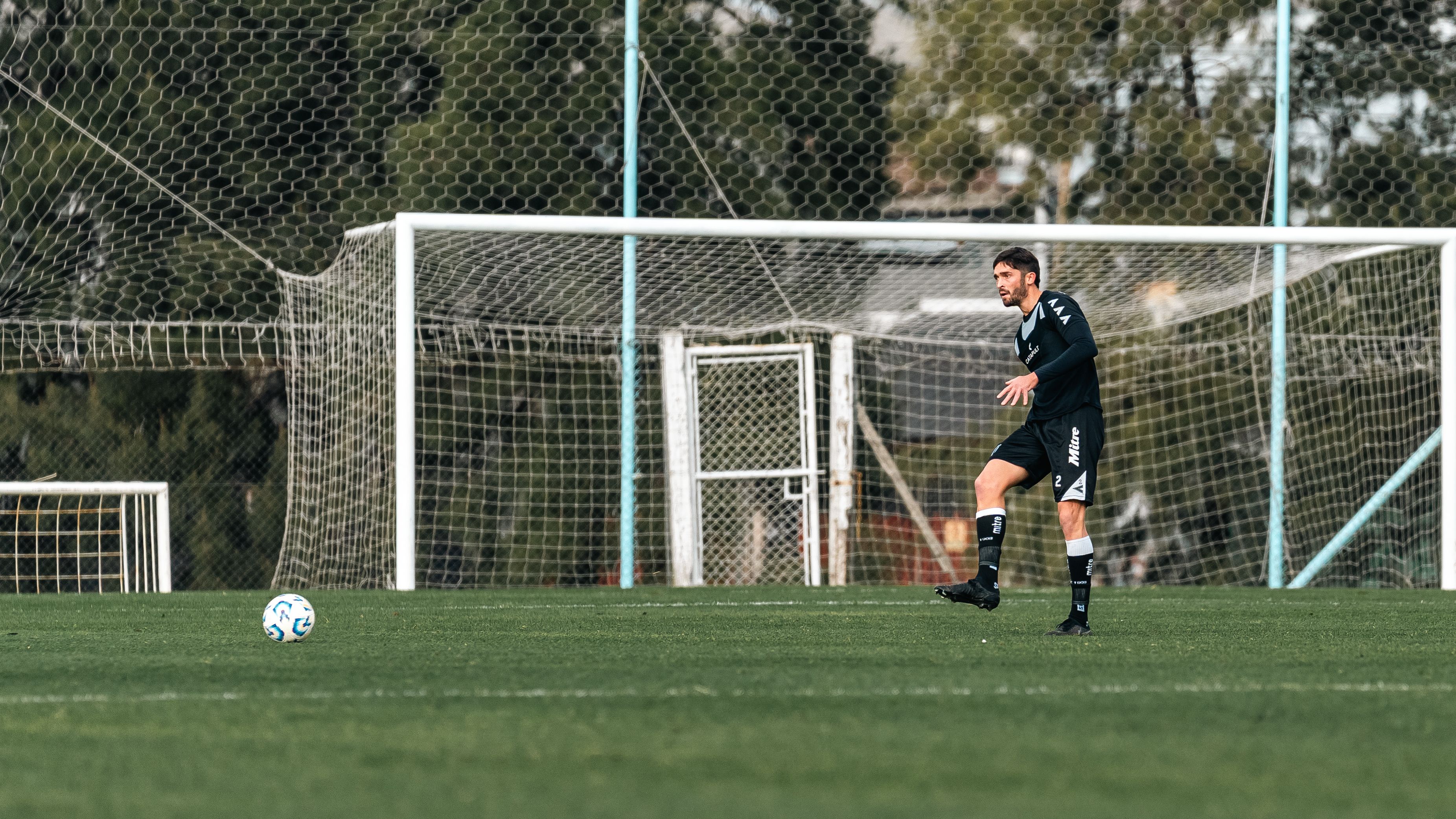 Soccer player in dark uniform preparing to kick the ball on a sunny outdoor field.