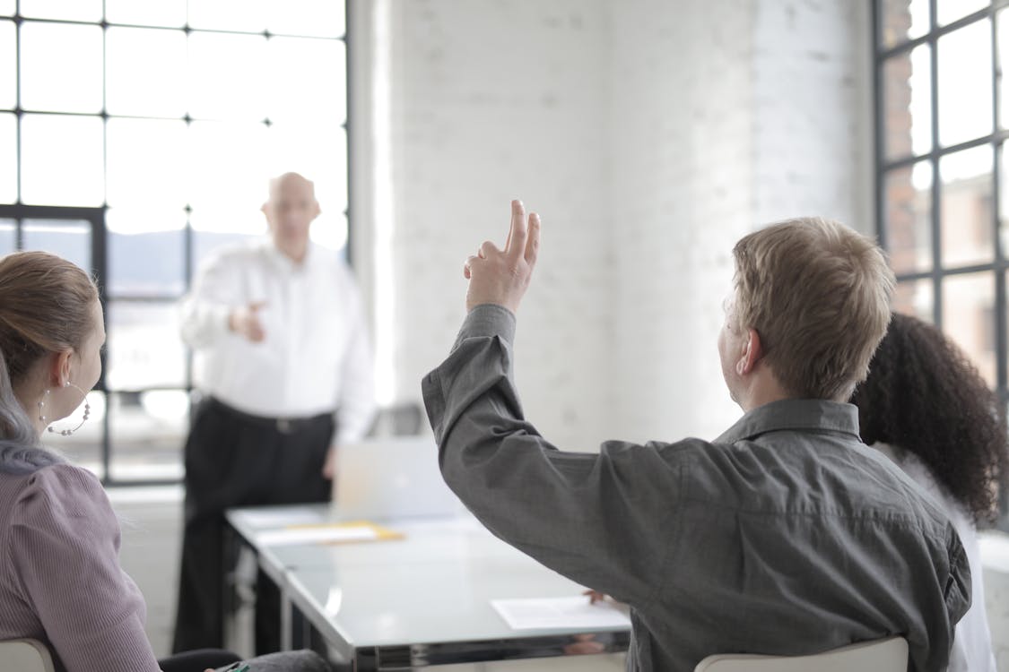 Free Male employee raising hand for asking question at conference in office boardroom Stock Photo