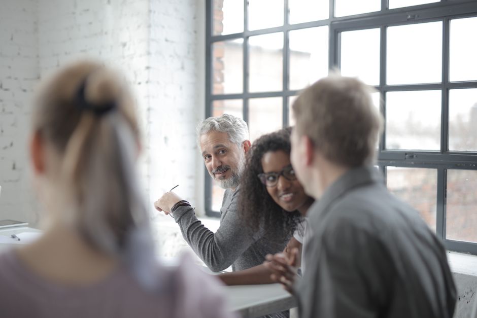 Cheerful diverse employees of different ages in casual wear having pleasant informal conversation while sitting together at table in office boardroom