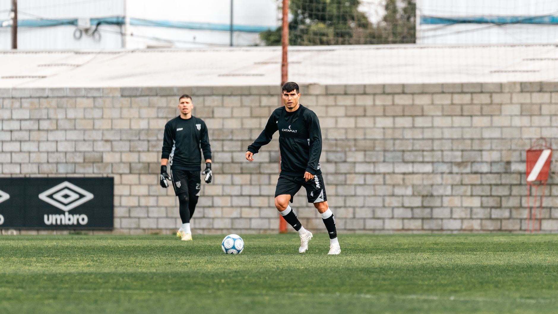 Two soccer players practicing on a field during daytime training session.
