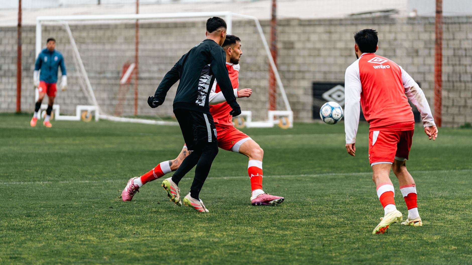 A coach timing sprint-to-dribble repetitions beside a tablet on a professional football training ground