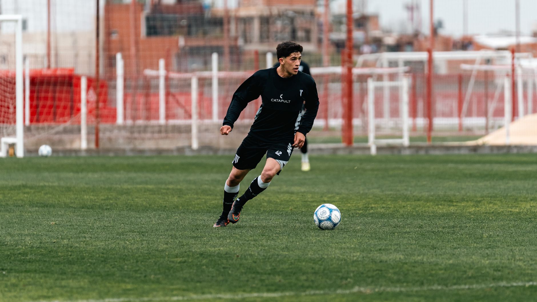 A focused footballer dribbling through cones on a wet training pitch, dawn light and precise footwork