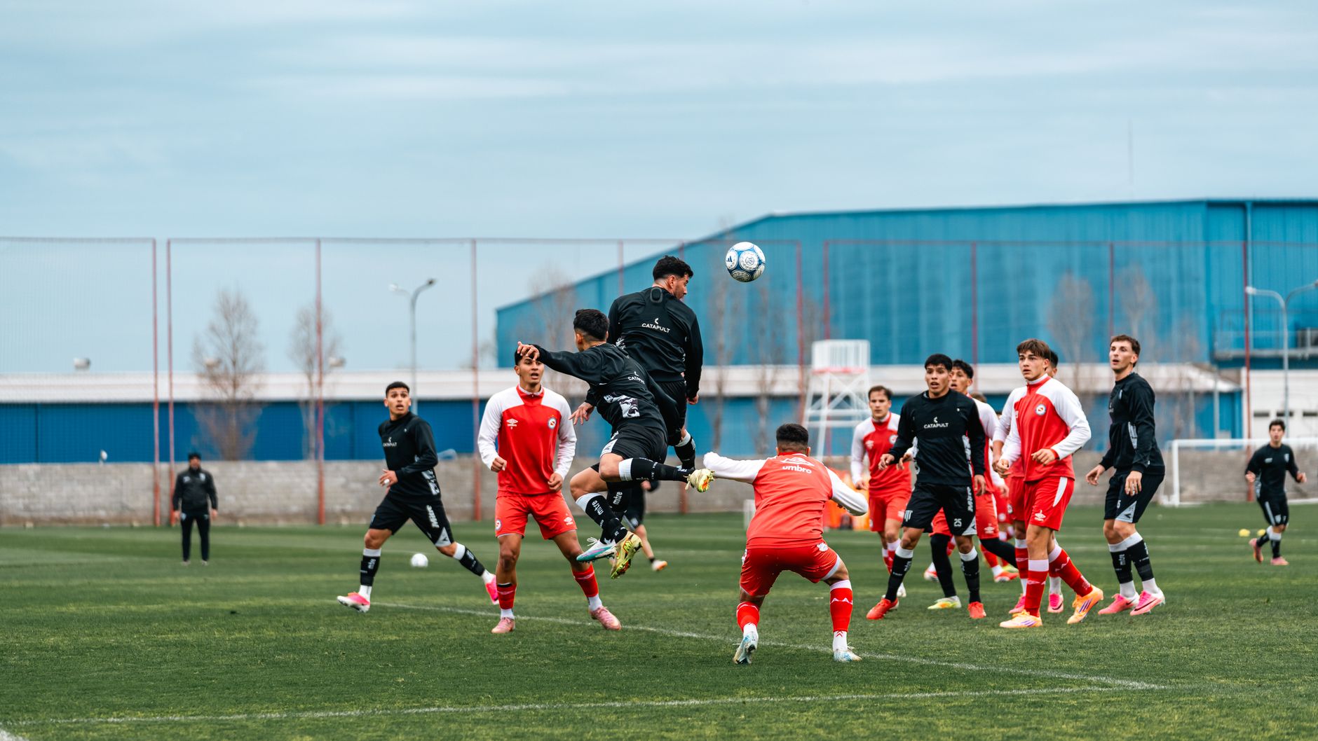 Soccer players in black and red kits compete intensely on an outdoor field.