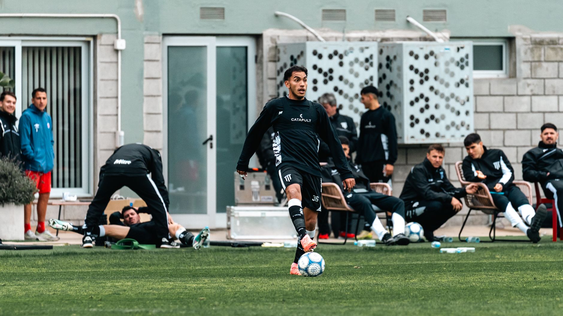a football coach recording dribbling times beside cones while players recover between intense repetitions