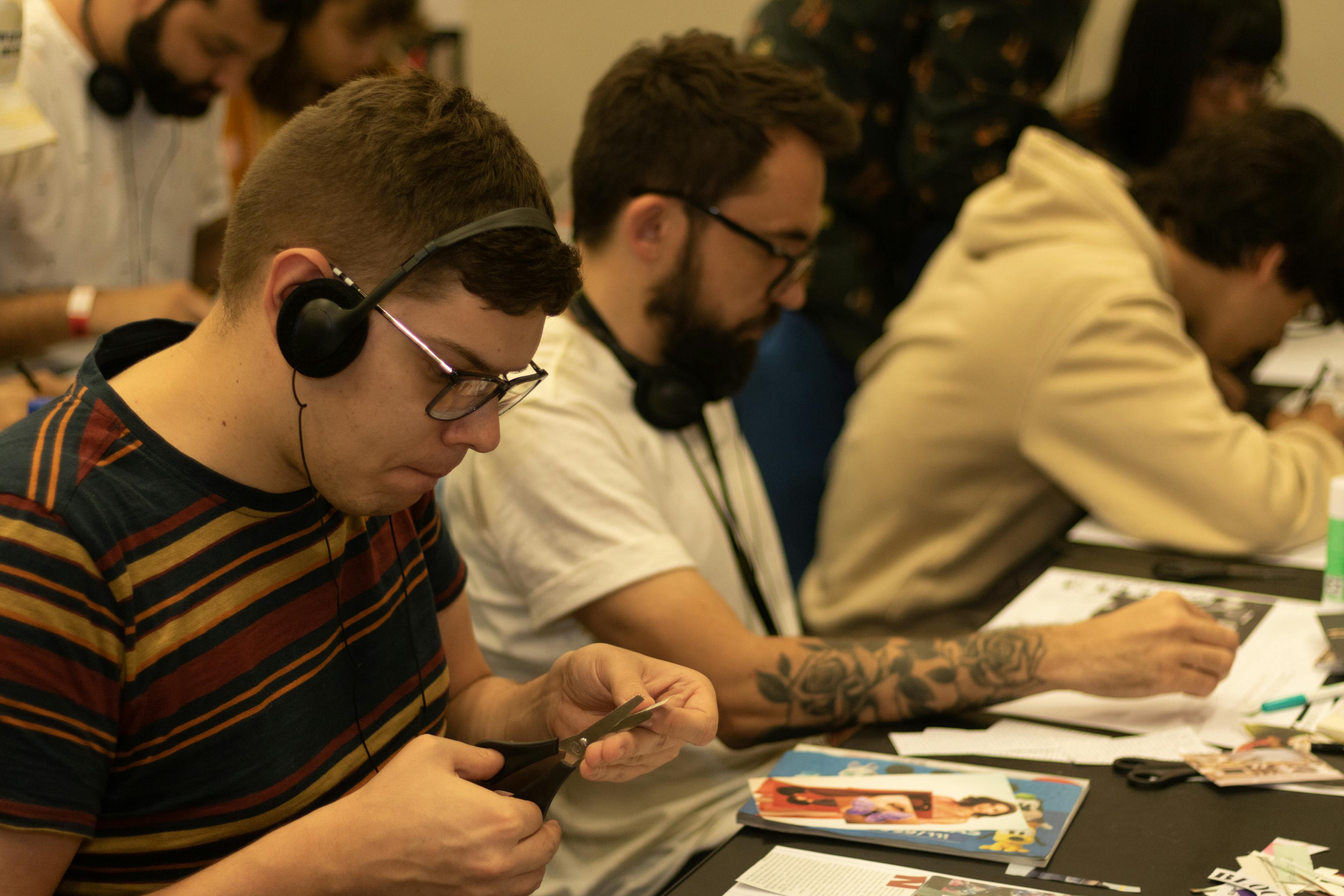 High angle of concentrated young students in casual clothes with headphones cutting paper while creating artwork during lesson