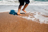 阳光明媚的海边，一个孩子高兴地跳上沙滩，在海沫中泼溅