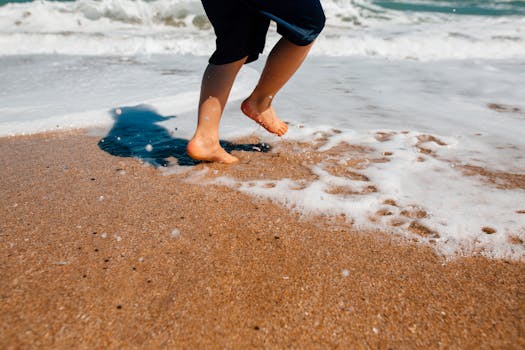 阳光明媚的海边，一个孩子高兴地在沙滩上跳跃，溅起阵阵海沫