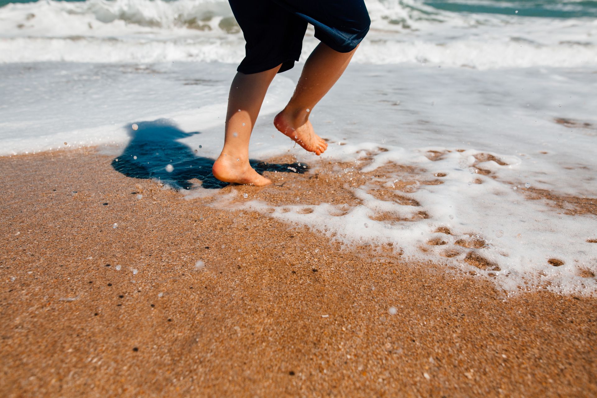 A child joyfully jumps on the sandy beach, splashing in the sea foam at a sunny seaside.