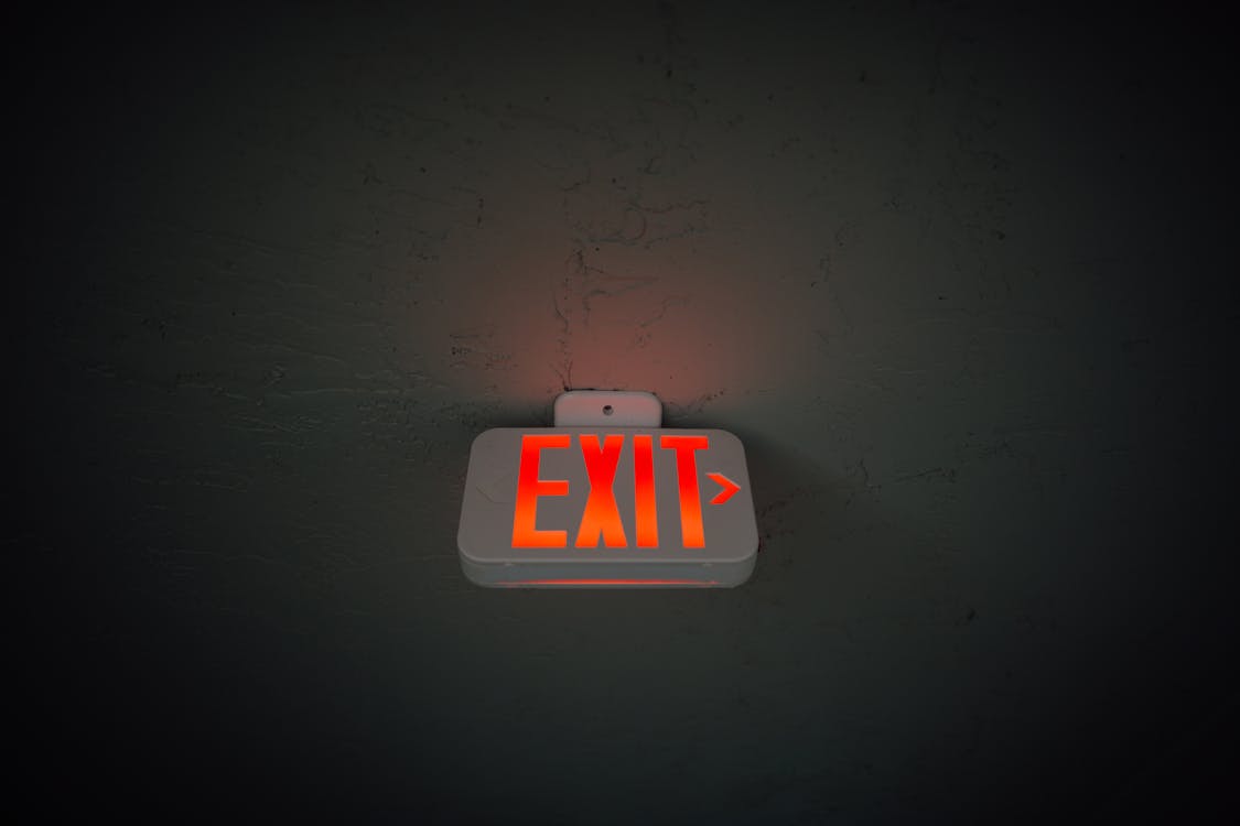 Free From below of illuminated exit sign hanging on gray concrete ceiling in dark room Stock Photo