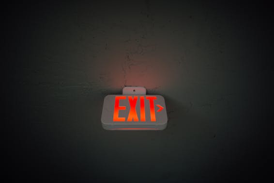 From below of illuminated exit sign hanging on gray concrete ceiling in dark room