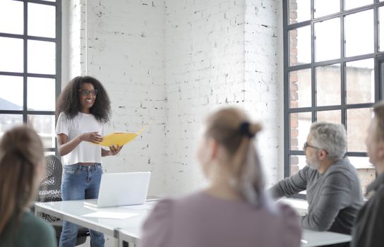 A diverse team engaged in a vibrant office meeting led by a woman presenting ideas.