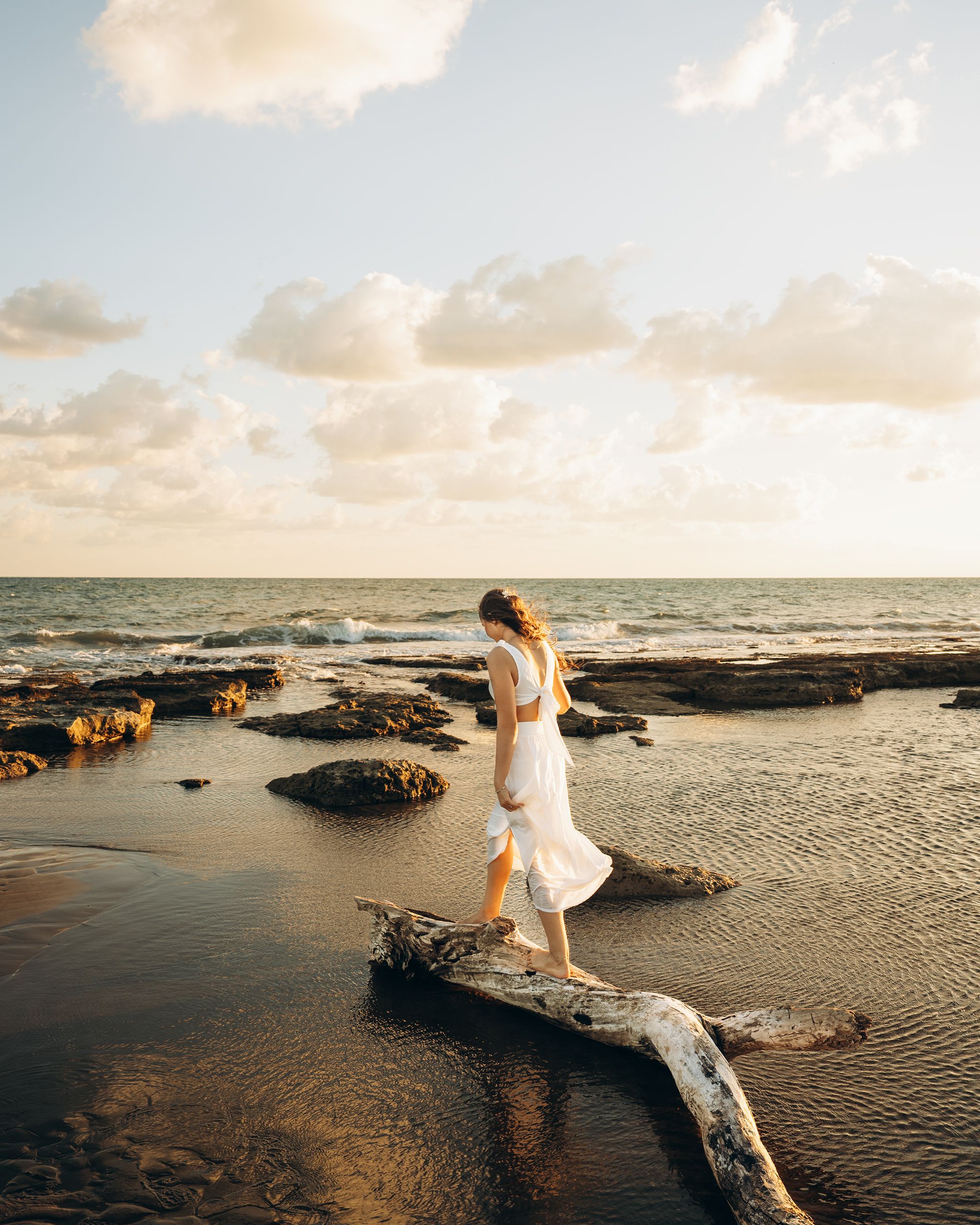 A bride in a white dress walks along a serene beach at sunset in Antalya, Türkiye.