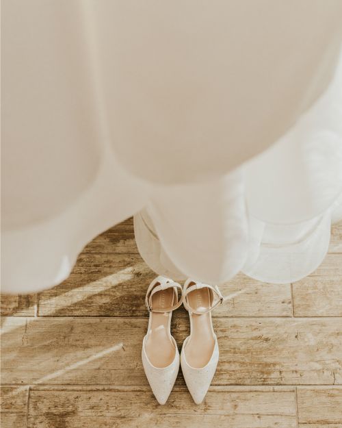 Free Elegant bridal shoes beneath a wedding dress in a sunlit room, capturing a moment of anticipation. Stock Photo