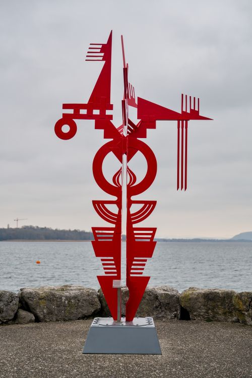 Free Vibrant red abstract sculpture set against a serene lakeside view. Stock Photo