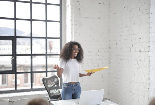 A cheerful young woman presenting in a modern office with large windows.