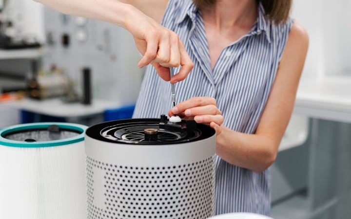 Close-up of a young woman using a screwdriver to repair an air purifier in a laboratory environment.